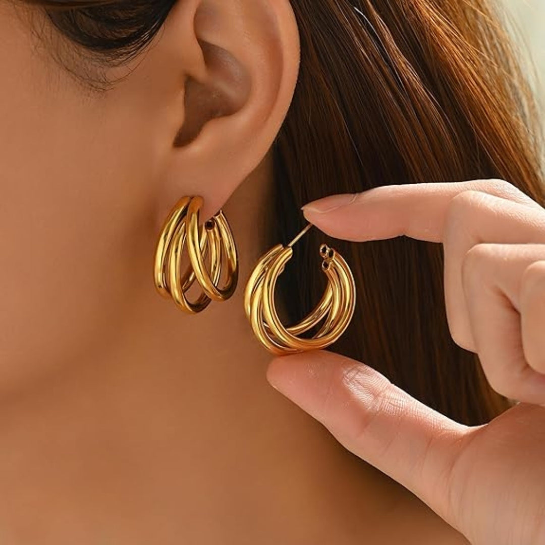 Close-up of triple hoop gold earrings shining under light.