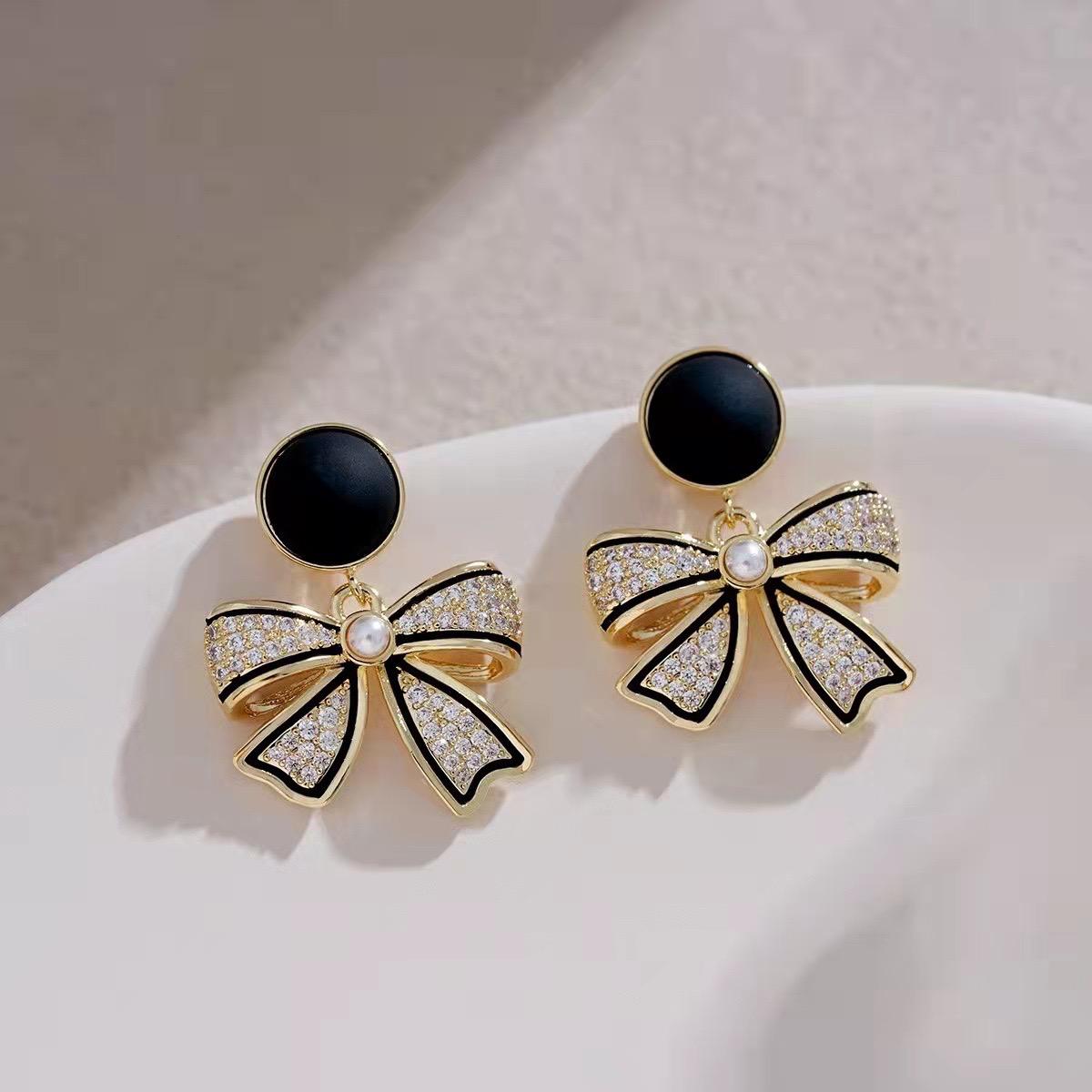 Elegant bow-shaped earrings with black studs, gold outline.